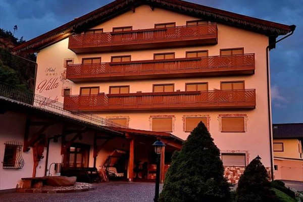 Duży hotel z drewnianymi balkonami i ogrodem w wieczornym oświetleniu.