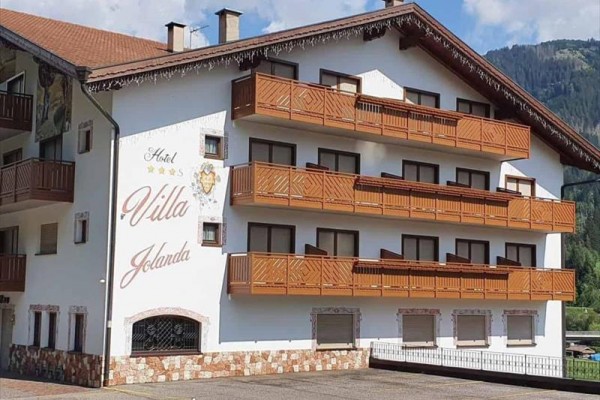 Biały budynek hotelu Villa Jolanda z drewnianymi balkonami i napisem na fasadzie.