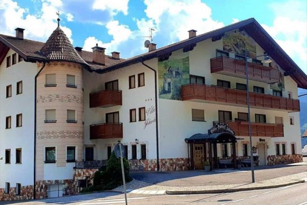 Budynek hotelu z drewnianymi balkonami i malowidłami na elewacji pod chmurami.