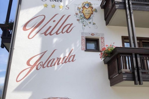 Boczna fasada hotelu Villa Jolanda z balkonem ozdobionym kwiatami.