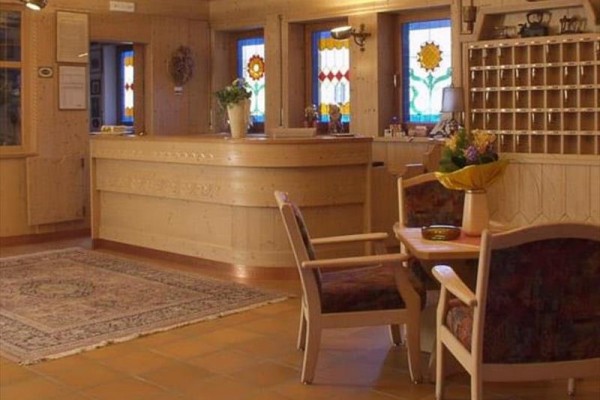 Recepcja hotelowa z drewnianymi meblami i kolorowymi witrażowymi oknami.