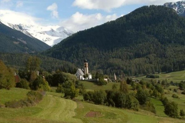 Malownicza wioska z kościołem otoczona górami i lasami.