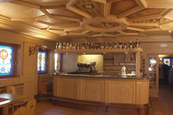 Drewniane wnętrze kawiarni z barem, butelkami alkoholu i witrażowymi oknami.