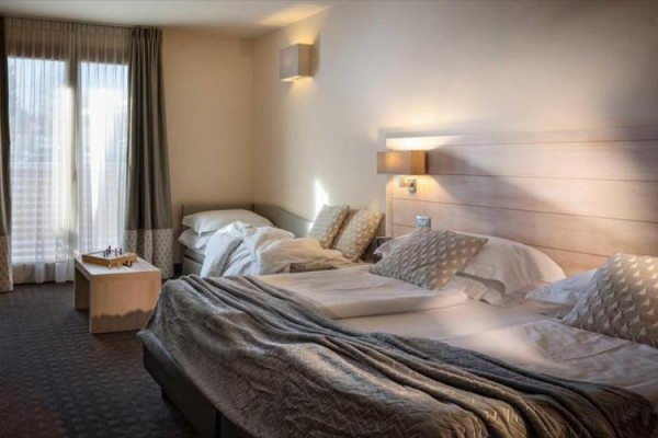 Przestronny pokój hotelowy z łóżkiem małżeńskim, dostawką i dużym oknem z zasłonami.