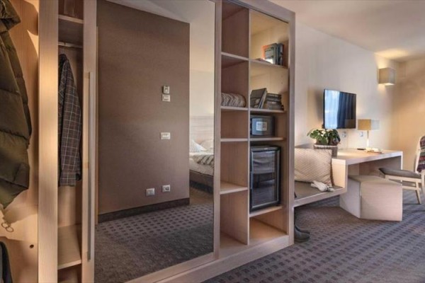 Nowoczesny pokój hotelowy z wbudowaną szafą, półkami, biurkiem i telewizorem na ścianie.