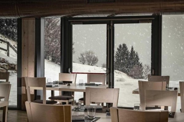 Restauracja z drewnianymi krzesłami i stołami z widokiem na zaśnieżony krajobraz.