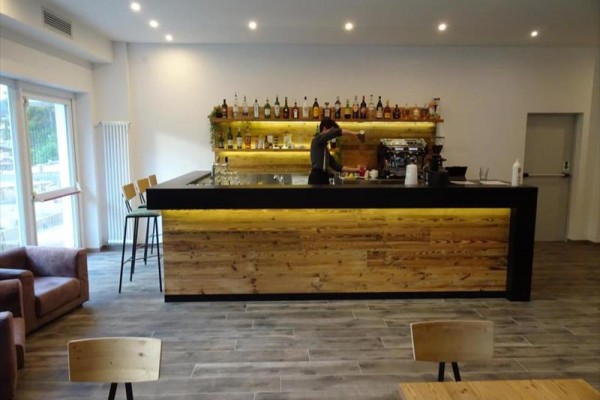 Nowoczesny bar z barmanem przygotowującym napój przed półką pełną butelek alkoholu.
