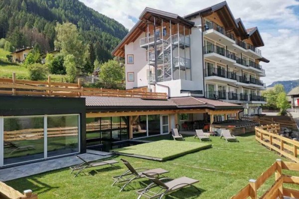 Górski hotel z tarasem i leżakami na zielonej trawie.