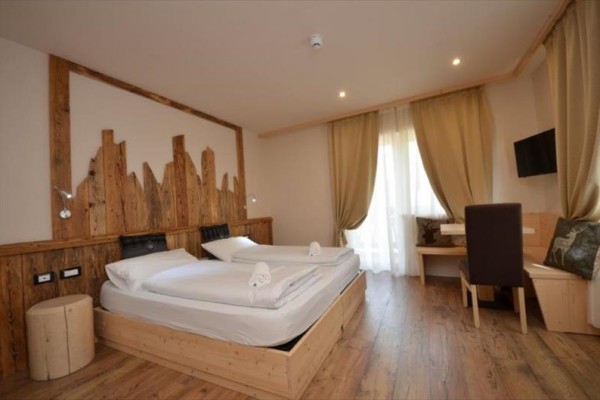 Przestronny pokój hotelowy z drewnianymi meblami, dwoma łóżkami, dużym oknem i zasłonami.