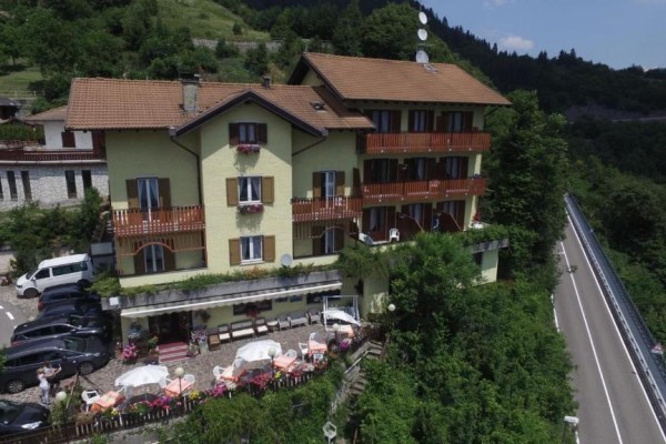 Budynek hotelu z żółtą elewacją i balkonami znajduje się w pagórkowatym terenie obok drogi.