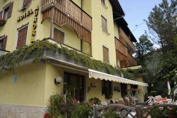 Żółty budynek hotelu Aurora z drewnianymi balkonami i ogrodem na zewnątrz.
