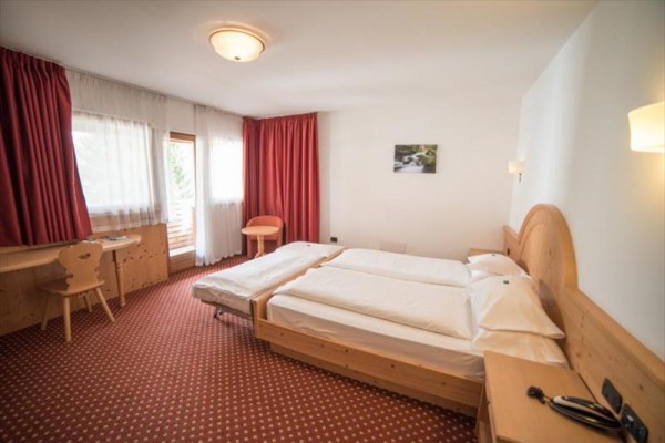 Pokój hotelowy z dwoma łóżkami, drewnianymi meblami i czerwonymi zasłonami.
