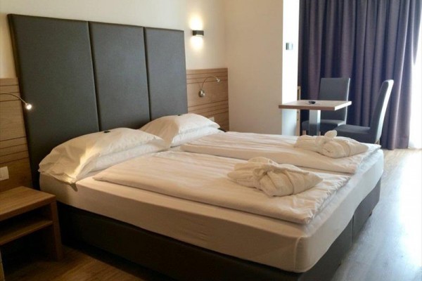 Nowoczesny pokój hotelowy z łóżkiem podwójnym, stolikami nocnymi i stołem z krzesłem.