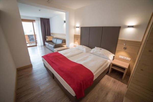 Nowoczesny pokój hotelowy z łóżkiem małżeńskim, czerwoną narzutą i balkonem.