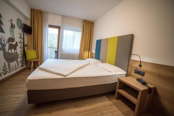Nowoczesny pokój hotelowy z podwójnym łóżkiem, kolorowym zagłówkiem i malowidłem zwierząt na ścianie.