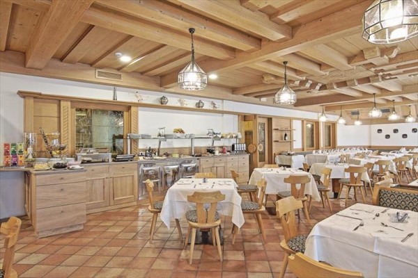 Przestronna restauracja z drewnianym wnętrzem i stołami jadalnymi przykrytymi białymi obrusami.