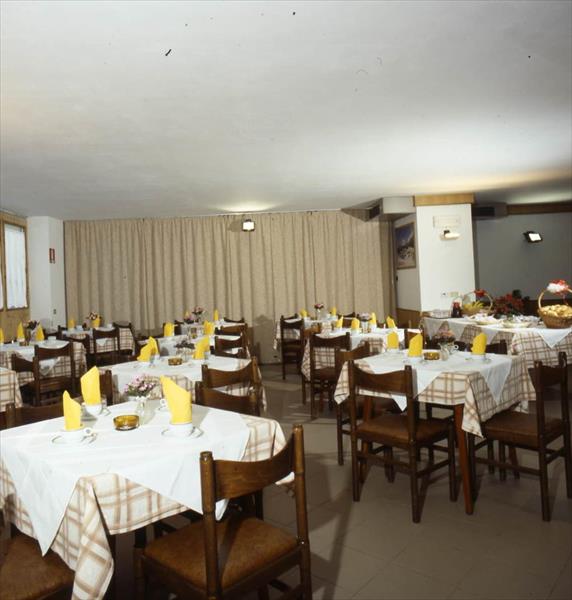 Restauracja z drewnianymi krzesłami i stołami przykrytymi białymi obrusami i żółtymi serwetkami.