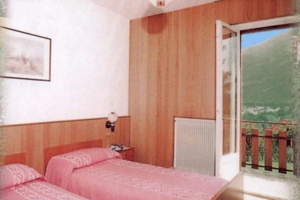 Pokój z dwoma łóżkami z różową pościelą i otwartymi drzwiami na balkon.