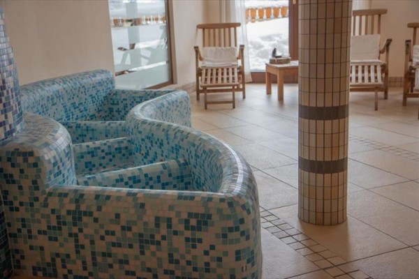 Pokój relaksacyjny spa z mozaikowymi leżankami i drewnianymi krzesłami.