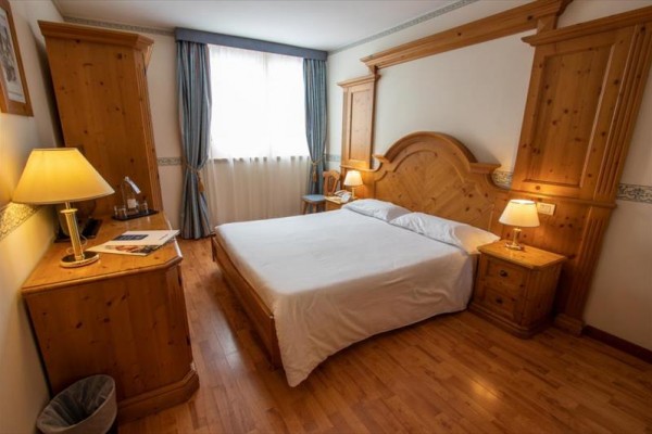 Pokój hotelowy z podwójnym łóżkiem i drewnianymi meblami.
