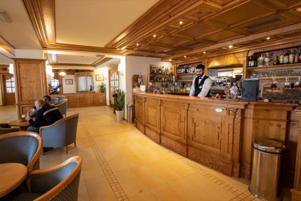 Drewniany bar z barmanem w eleganckim wnętrzu z gośćmi siedzącymi w fotelach.