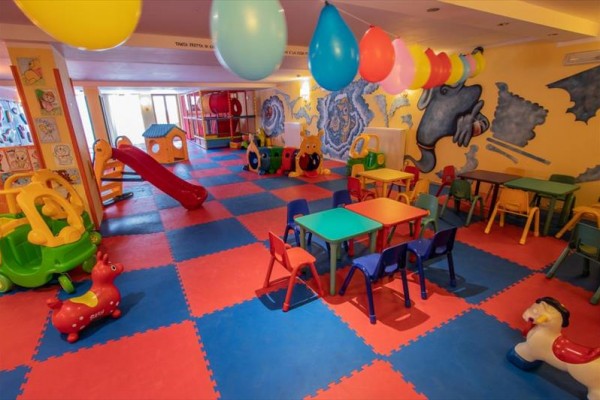 Sala zabaw dla dzieci z kolorowymi stolikami, krzesełkami i zabawkami.