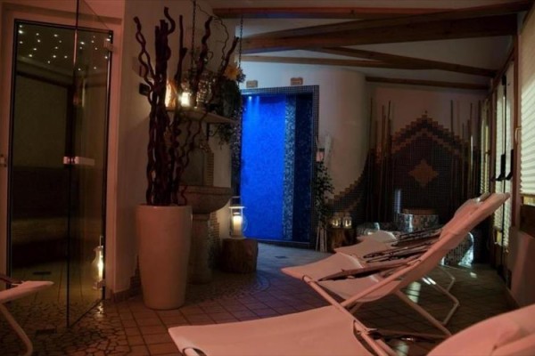 Sala relaksacyjna z leżakami i przyciemnionym oświetleniem obok niebiesko podświetlonego wodospadu.