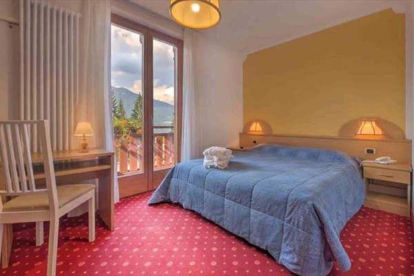 Pokój hotelowy z podwójnym łóżkiem, niebieską narzutą i widokiem na góry.