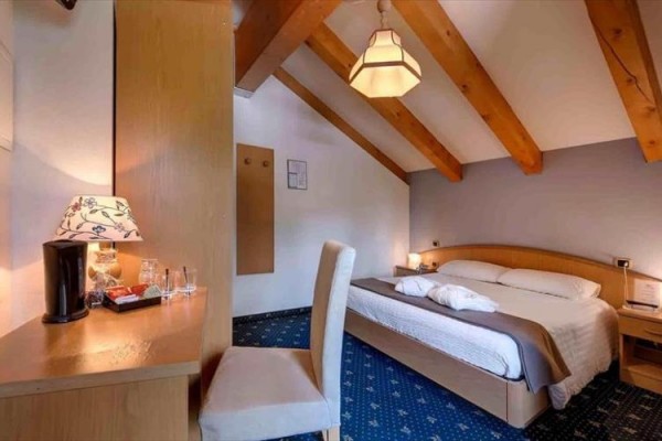 Pokój hotelowy na poddaszu z łóżkiem małżeńskim i biurkiem.