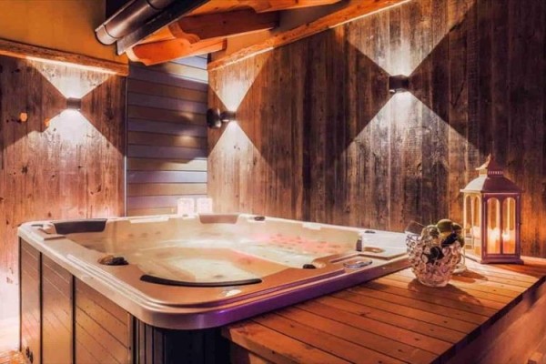 Wewnętrzne jacuzzi otoczone drewnianymi panelami z oświetleniem i lampionem na stole.