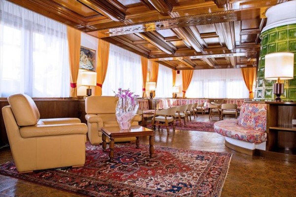 Stylowy salon z drewnianym sufitem, skórzanymi fotelami, kwiatową poduszką i kolorowym dywanem.