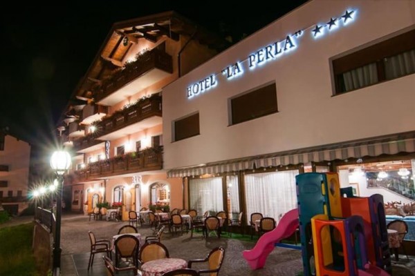 Nocny widok na oświetlony hotel z zewnętrznymi miejscami do siedzenia i placem zabaw.