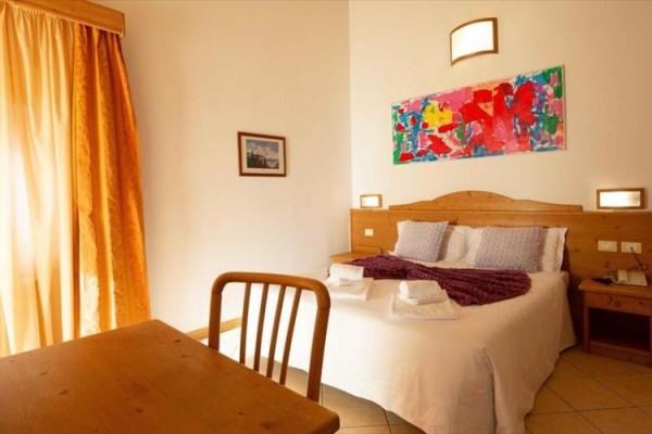 Pokój hotelowy z łóżkiem małżeńskim, drewnianymi meblami i kolorowym obrazem na ścianie.