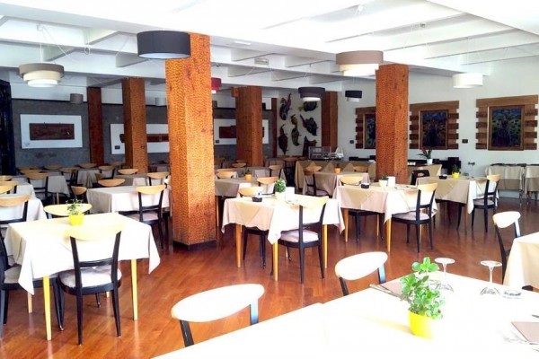 Restauracja z drewnianymi kolumnami i stołami przykrytymi białymi obrusami.