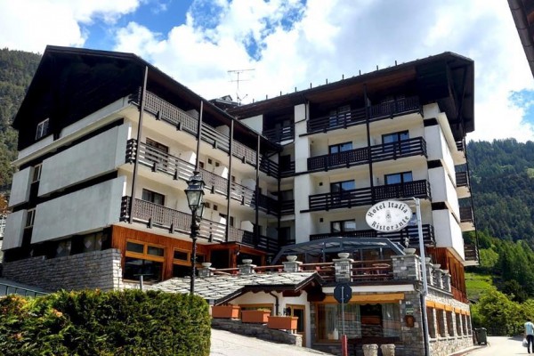 Budynek hotelowy z balkonami w górskiej scenerii otoczonej lasami.