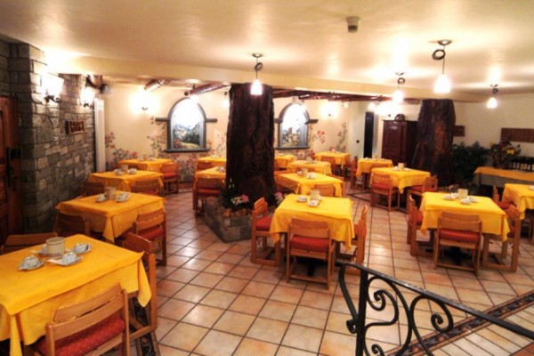 Restauracja z ceramiczną podłogą, kamiennymi ścianami i stołami z żółtymi obrusami.