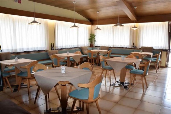 Restauracja z jasnymi drewnianymi meblami i białymi zasłonami.