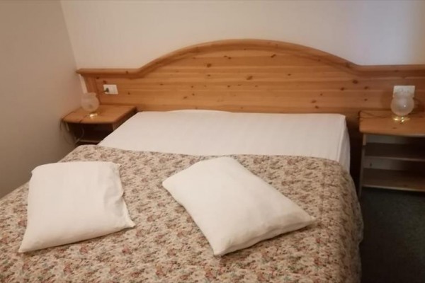 Łóżko małżeńskie z drewnianym zagłówkiem i kwiecistą narzutą.