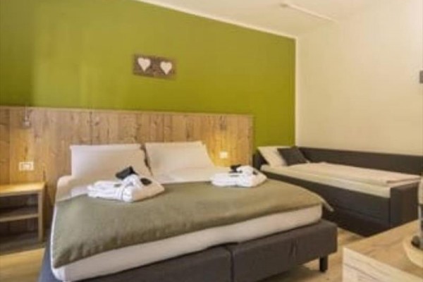 Przytulny pokój hotelowy z łóżkiem małżeńskim, pojedynczym łóżkiem i zieloną ścianą.