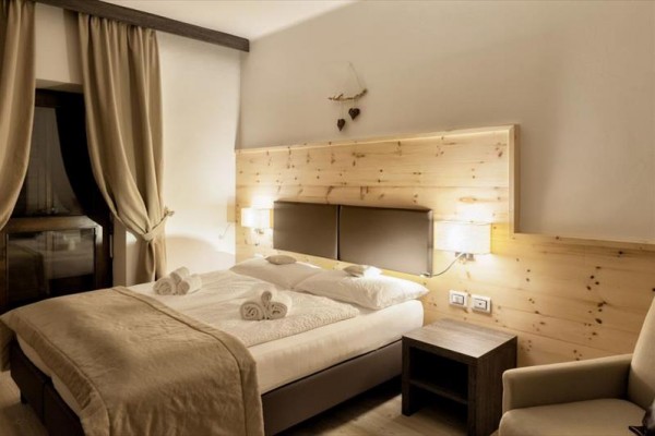 Nowoczesny pokój hotelowy z łóżkiem małżeńskim, drewnianą boazerią i zasłonami przy oknie.