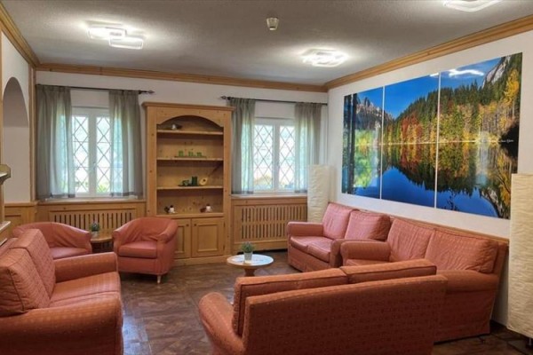 Salon z pomarańczowymi sofami i obrazem lasu nad jeziorem na ścianie.