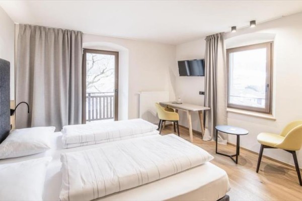 Jasny pokój hotelowy z dwoma łóżkami, biurkiem, telewizorem i balkonem.
