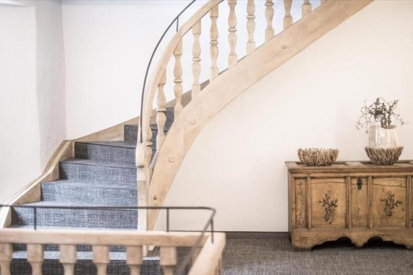 Drewniane schody z balustradą obok zabytkowej szafki z dekoracjami.
