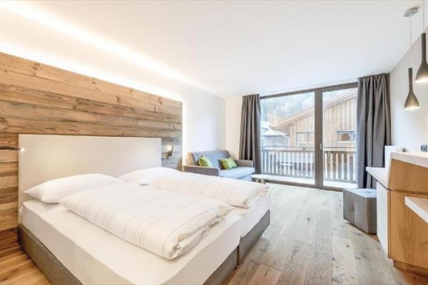 Nowoczesny pokój hotelowy z łóżkiem małżeńskim, sofą i widokiem na balkon.