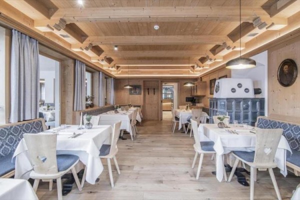 Wnętrze restauracji z drewnianą boazerią, białymi obrusami i wiklinowymi krzesłami.