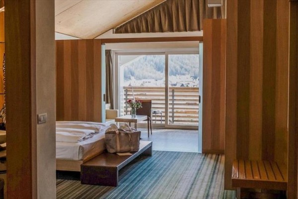 Nowoczesny pokój hotelowy z drewnianymi meblami, widokiem na góry i balkonem z fotelem.