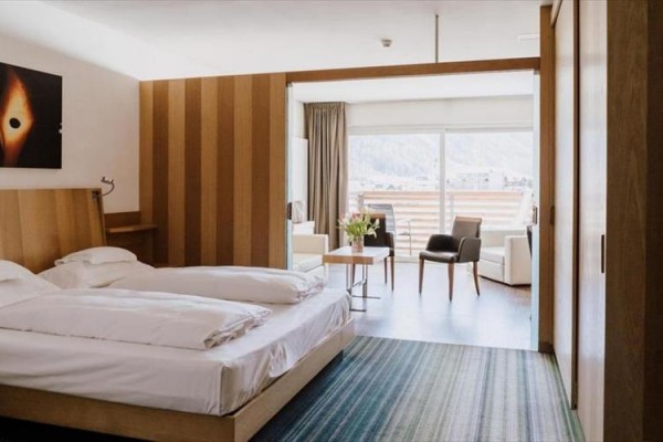 Pokój hotelowy z łóżkiem małżeńskim, stołem i krzesłami, balkonem oraz widokiem na góry.
