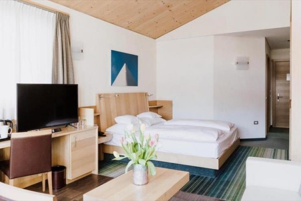 Nowoczesny pokój hotelowy z łóżkiem, telewizorem, biurkiem i bukietem tulipanów.