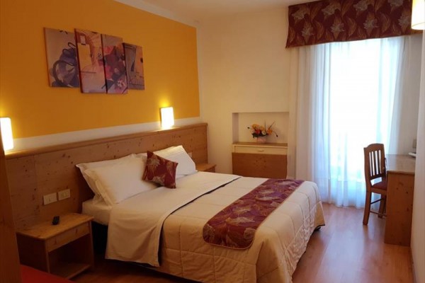 Przytulny pokój hotelowy z podwójnym łóżkiem, drewnianymi meblami i oknem z zasłonami.