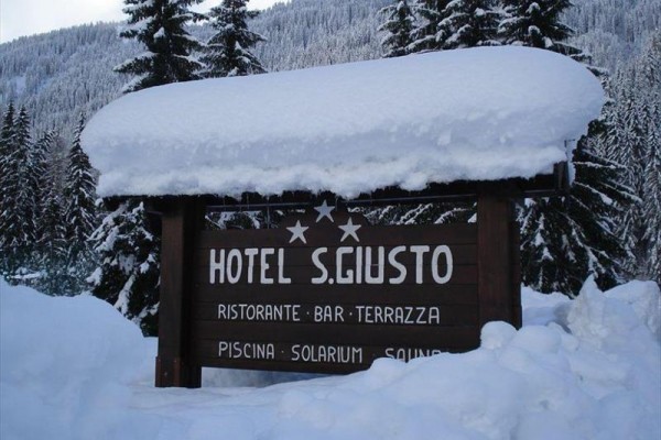 Drewniana tablica hotelu S. Giusto pokryta śniegiem w zimowym krajobrazie.
